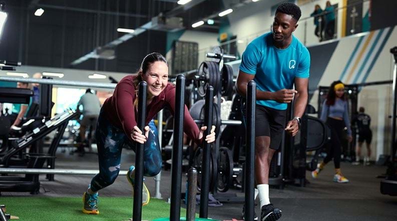 Lady pushing sled alongside personal trainer