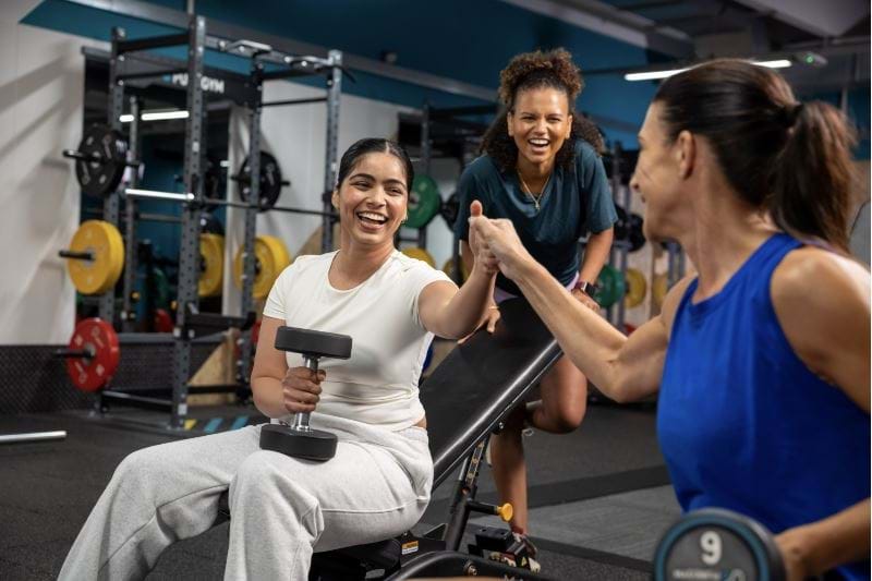 Three female PureGym members laughing and fist pumping